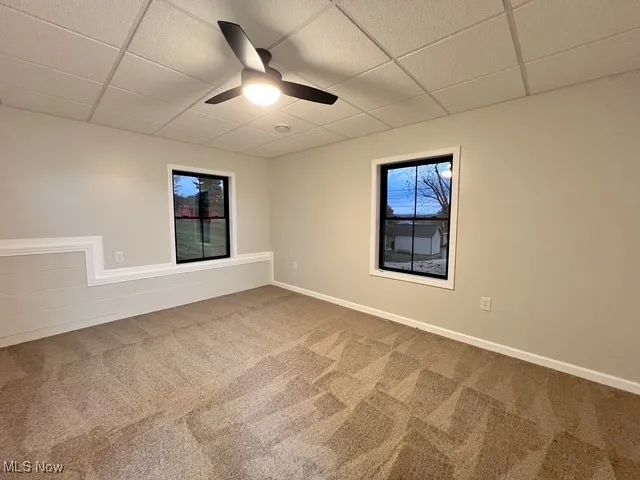 Empty room with a drop ceiling, carpet, and a ceiling fan