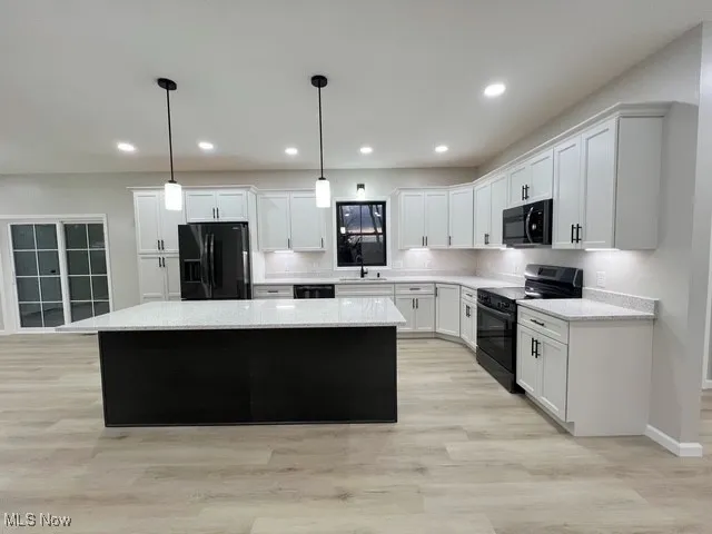 Kitchen featuring a kitchen island, black appliances, hanging light fixtures, white cabinets, and light wood-style floors