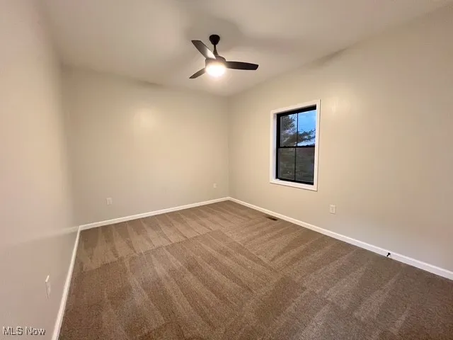 Carpeted spare room featuring baseboards and ceiling fan