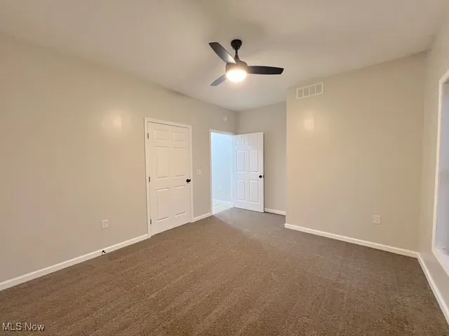 Unfurnished room featuring dark carpet and a ceiling fan