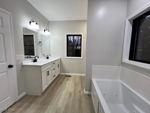 Full bathroom featuring a jetted tub, double vanity, and light wood finished floors