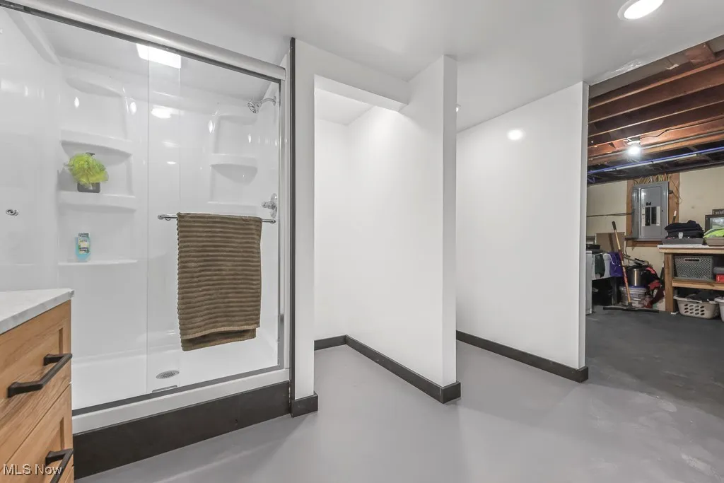 Bathroom with finished concrete flooring, a shower stall, electric panel, and vanity