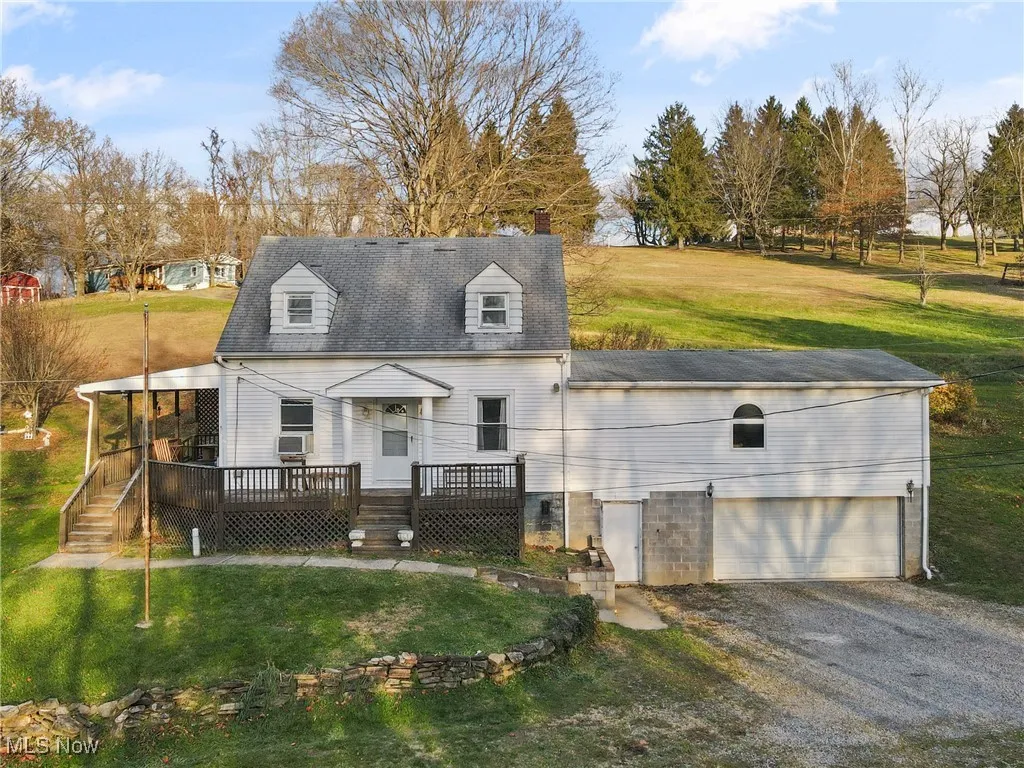 Cape cod home featuring a front yard, driveway, a deck, a shingled roof, and a garage