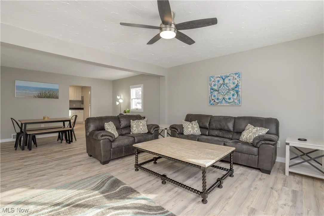 Living room featuring light wood-style flooring, a textured ceiling, and ceiling fan
