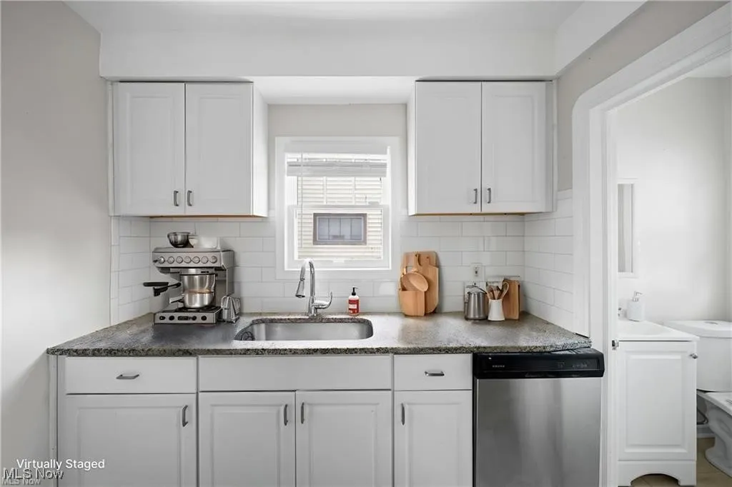 Kitchen with white cabinets, dishwasher, backsplash, and dark stone counters