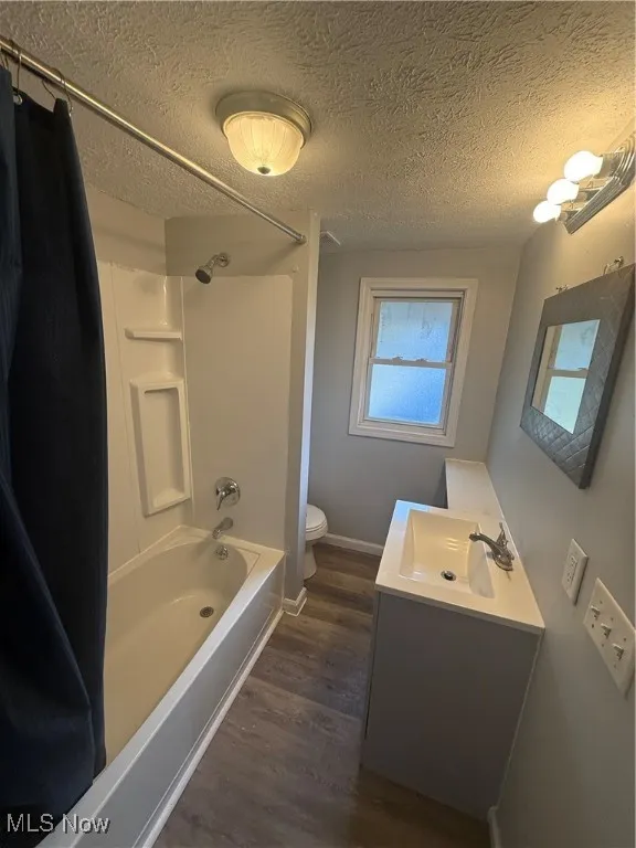 Full bath with shower / bath combo, vanity, a textured ceiling, and dark wood-style floors