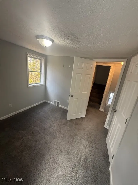 Unfurnished bedroom with dark colored carpet and a textured ceiling