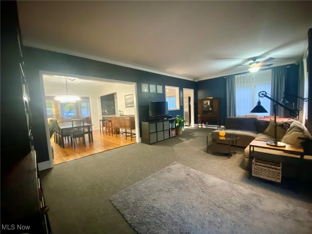 Carpeted living room featuring a ceiling fan and crown molding