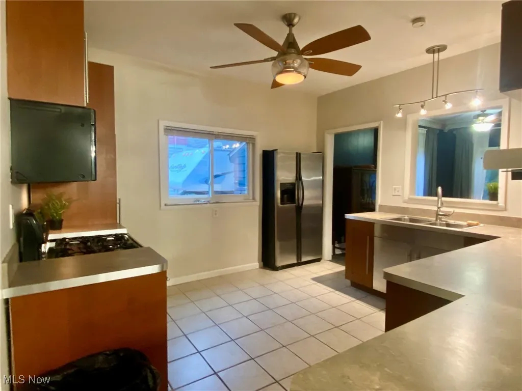 Kitchen with stainless steel fridge, light tile patterned floors, light countertops, ceiling fan, and gas stove