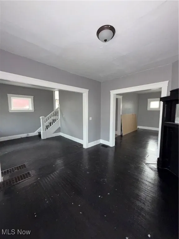 Unfurnished living room featuring dark wood-style flooring and stairway