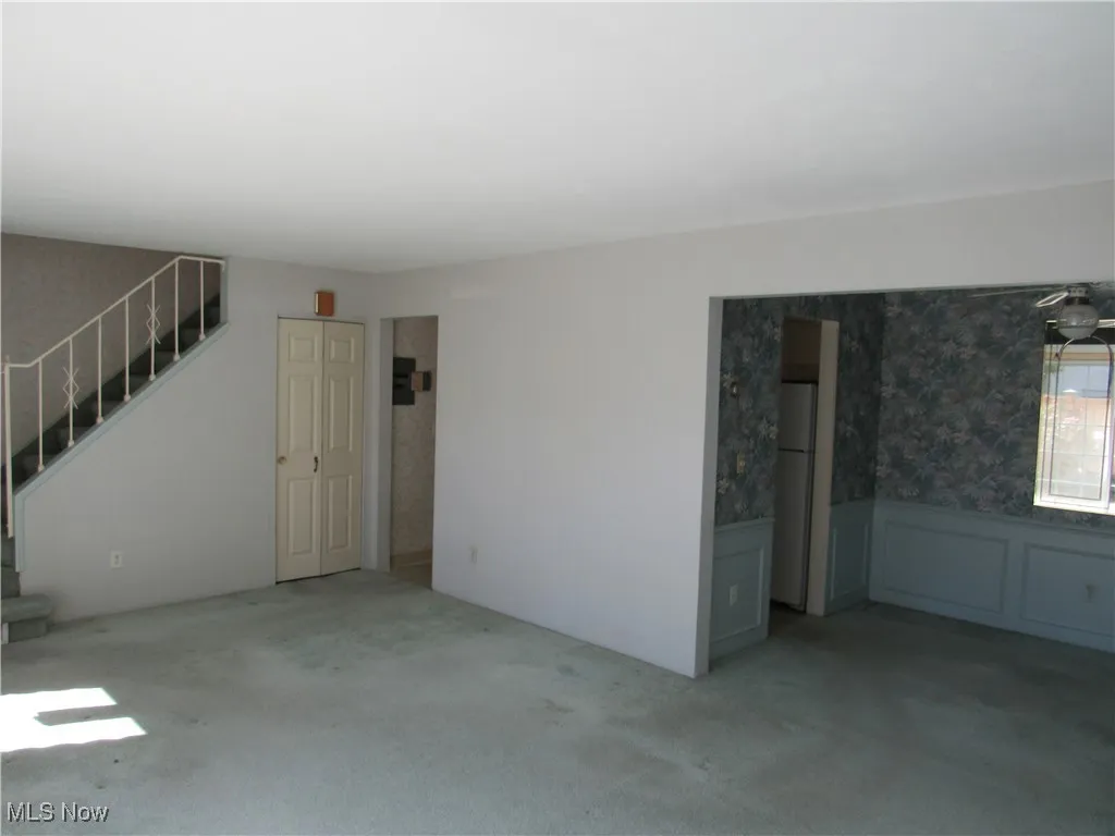 Unfurnished living room with a wainscoted wall, wallpapered walls, carpet flooring, and stairs