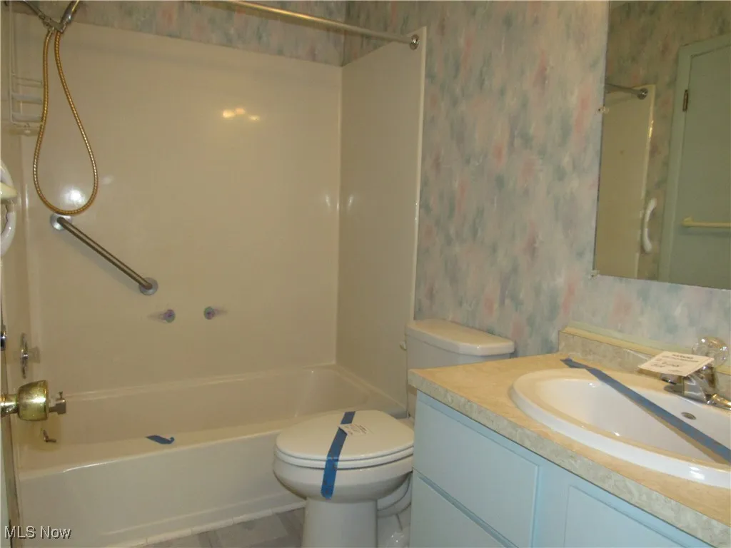 Full bathroom featuring wallpapered walls, vanity, shower / bathtub combination, and tile patterned flooring