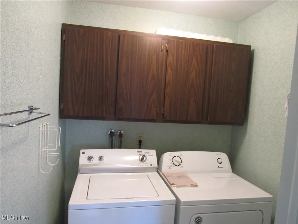 Laundry room with a textured wall, cabinet space, and washing machine and dryer