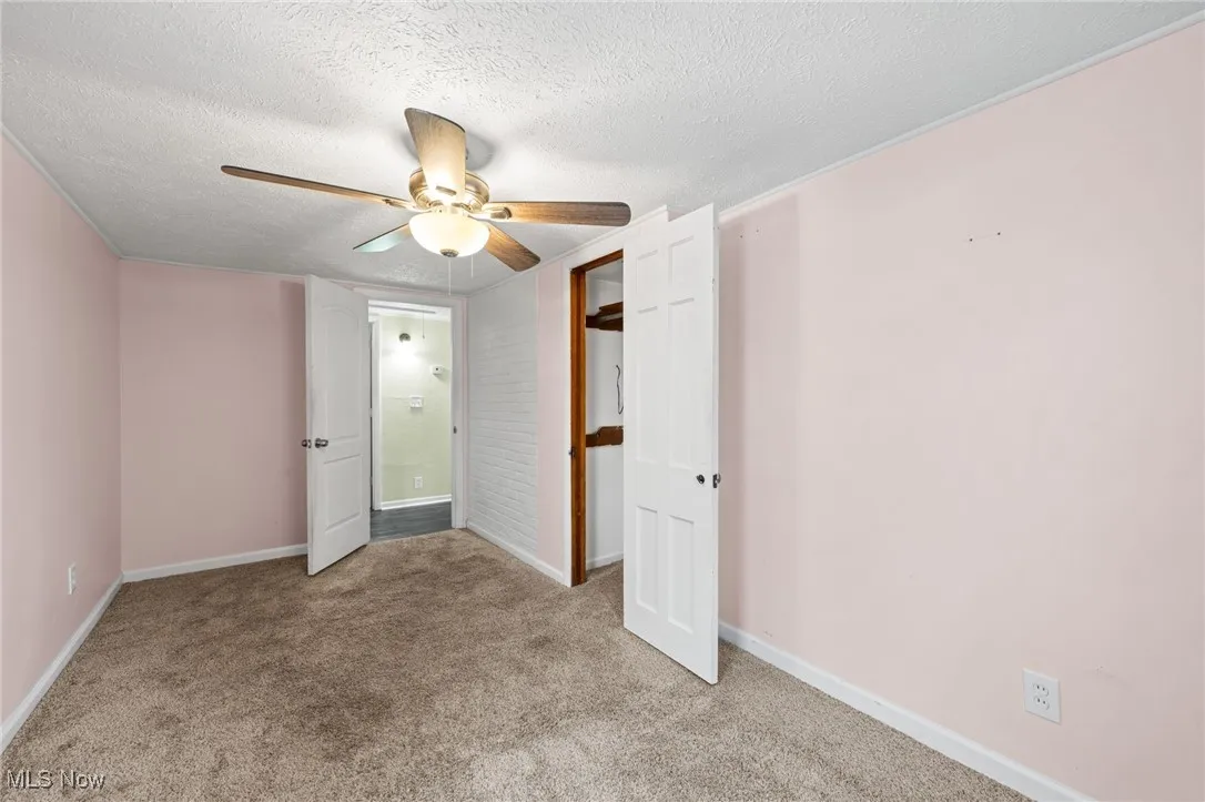 Unfurnished bedroom with a textured ceiling, light colored carpet, and ceiling fan