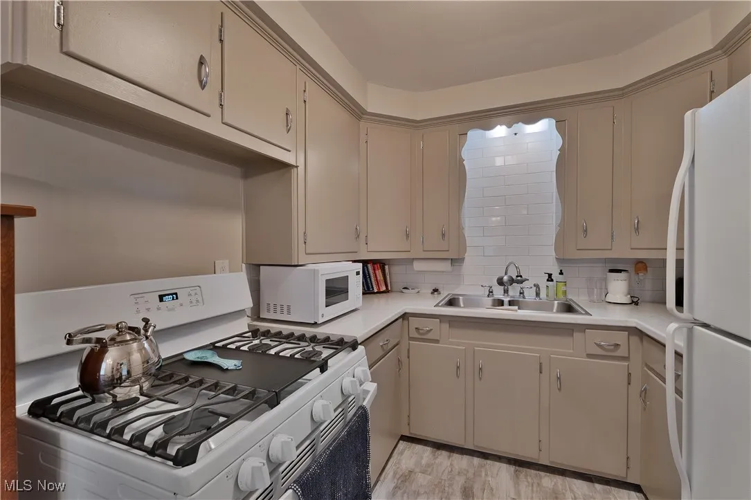 Kitchen with white appliances, light countertops, cream cabinets, tasteful backsplash, and light wood finished floors