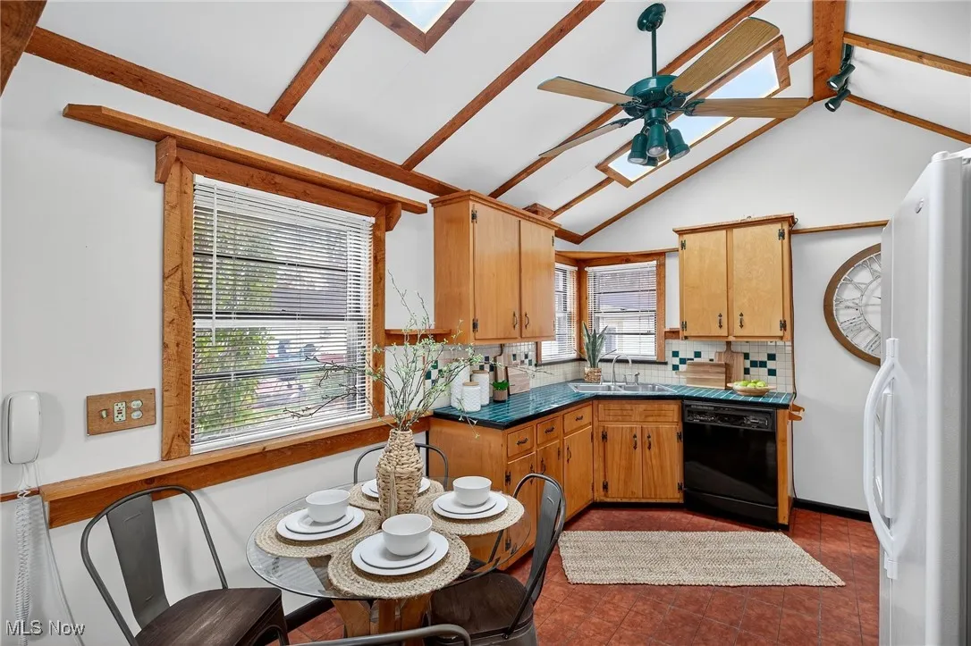 Kitchen featuring freestanding refrigerator, black dishwasher, decorative backsplash, ceiling fan, and brown cabinets