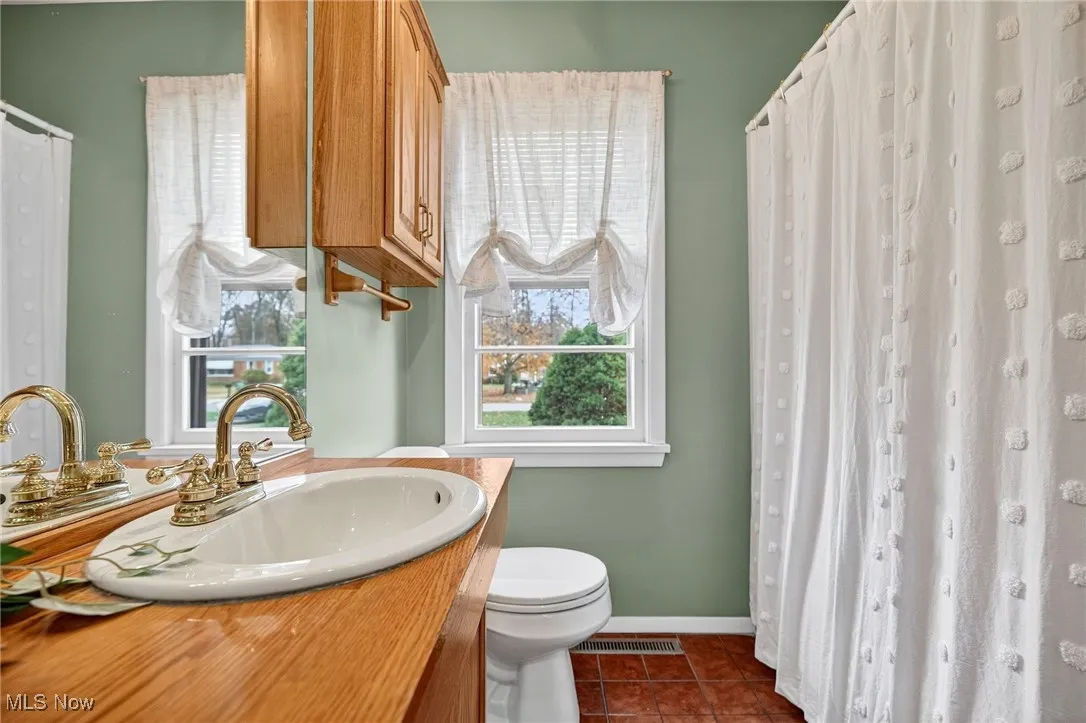 Bathroom with a shower with curtain, healthy amount of natural light, dark tile patterned flooring, and vanity