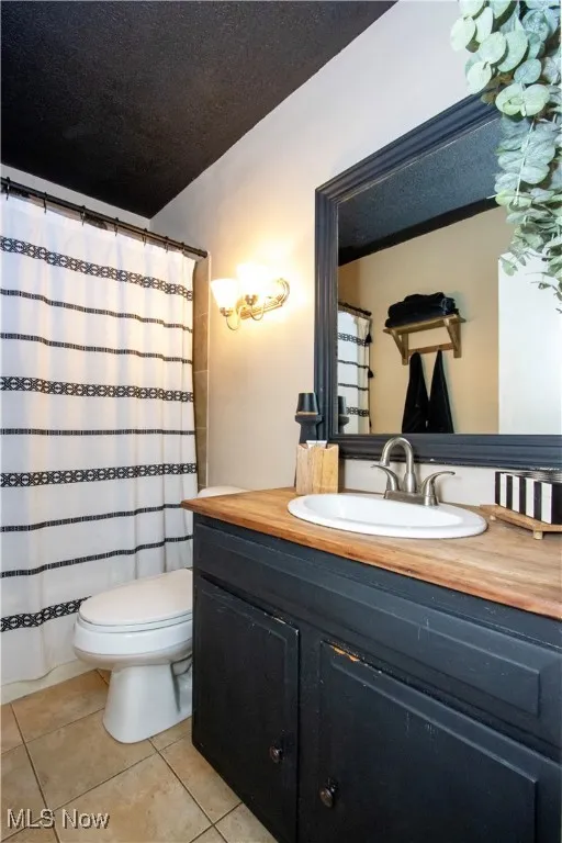 Bathroom with vanity, curtained shower, light tile patterned floors, and a textured ceiling