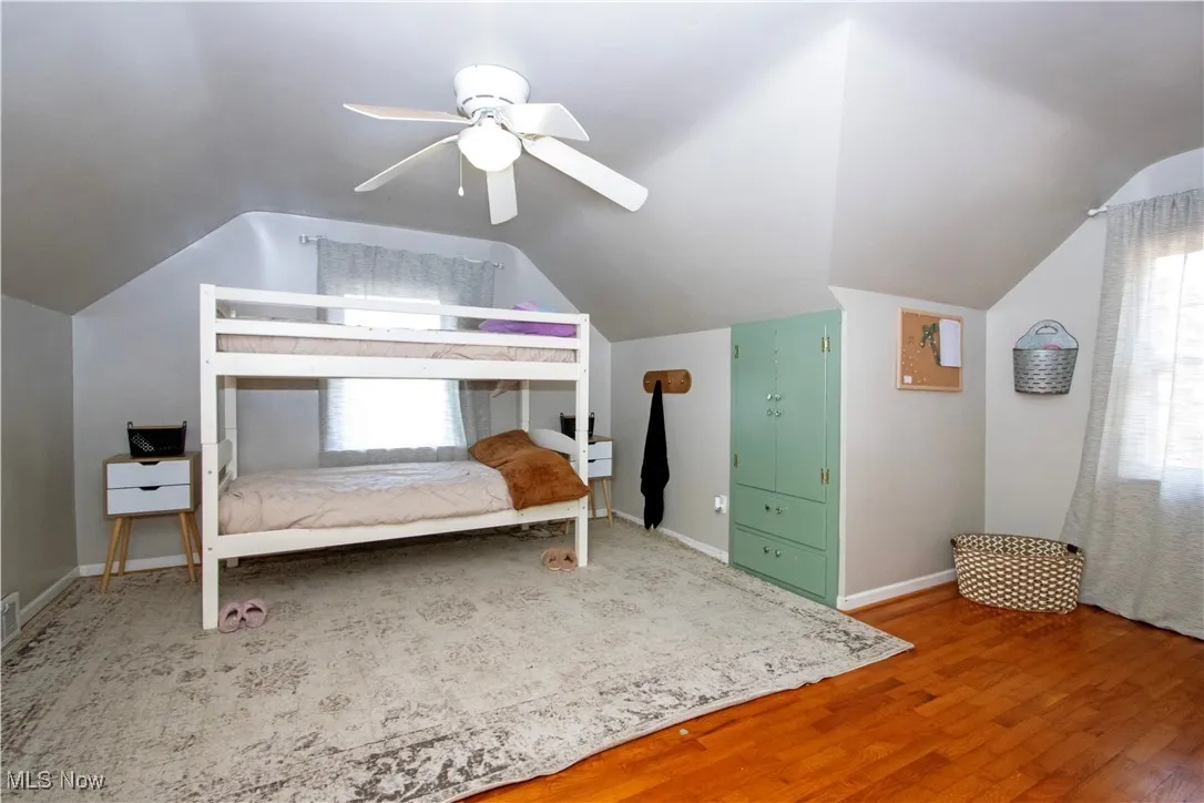 Bedroom featuring wood finished floors, lofted ceiling, multiple windows, and a ceiling fan