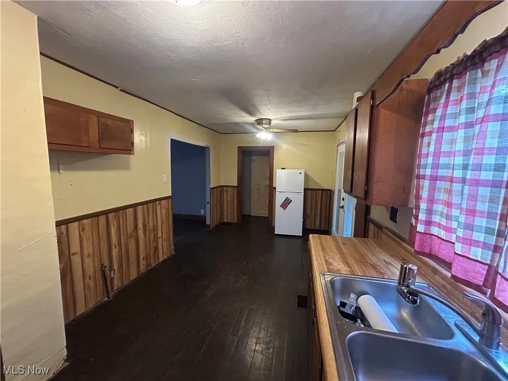 Kitchen with dark wood finished floors, brown cabinetry, wainscoting, freestanding refrigerator, and a textured ceiling
