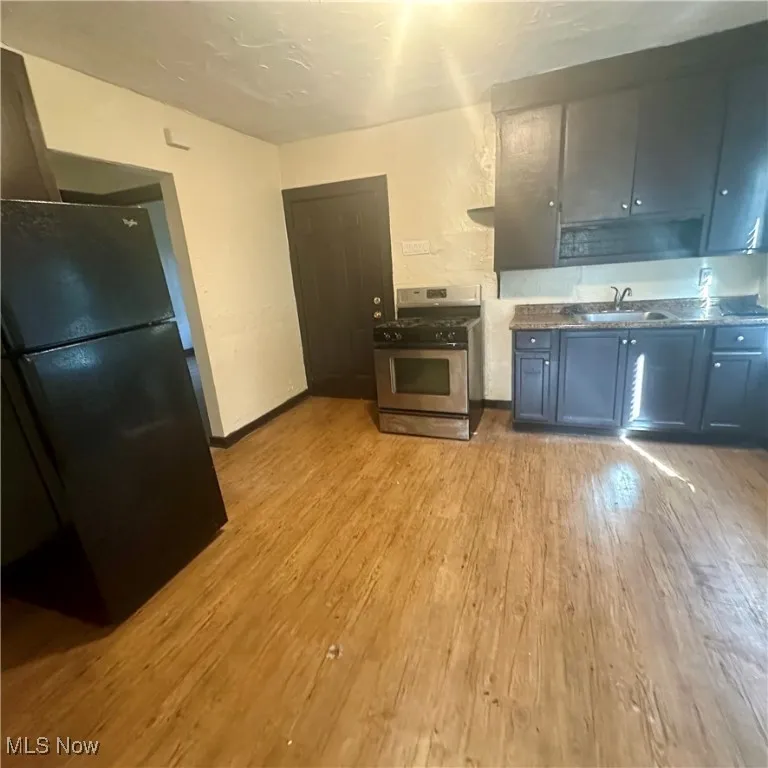 Kitchen with freestanding refrigerator, light wood-style floors, stainless steel range with gas stovetop, and dark stone countertops