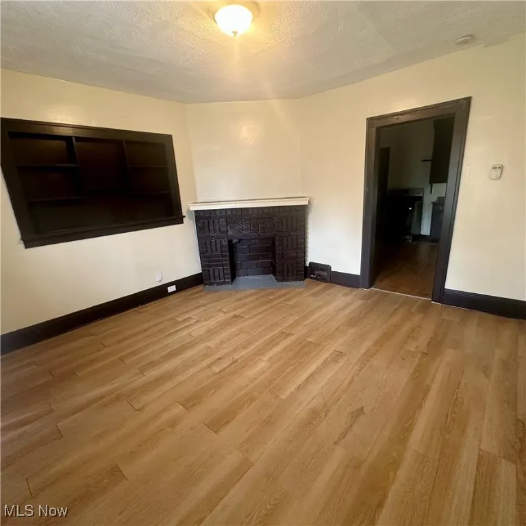 Unfurnished living room with a textured ceiling, light wood-type flooring, and a fireplace