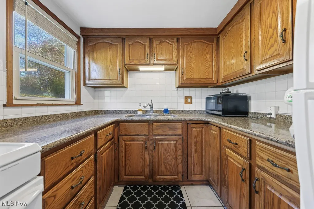 Kitchen with backsplash, brown cabinets, freestanding refrigerator, and light tile patterned floors