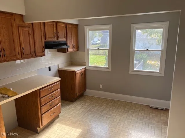 Kitchen with brown cabinetry, light countertops, tasteful backsplash, and brick patterned floors