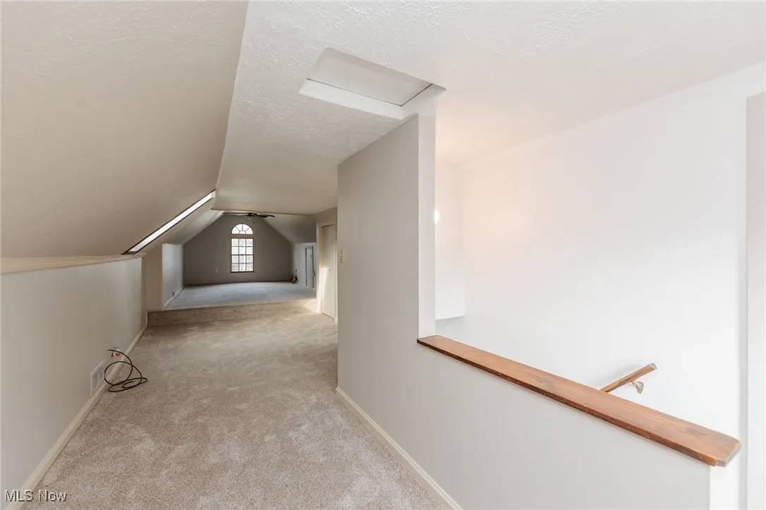Additional living space featuring light carpet, a textured ceiling, lofted ceiling, attic access, and a ceiling fan