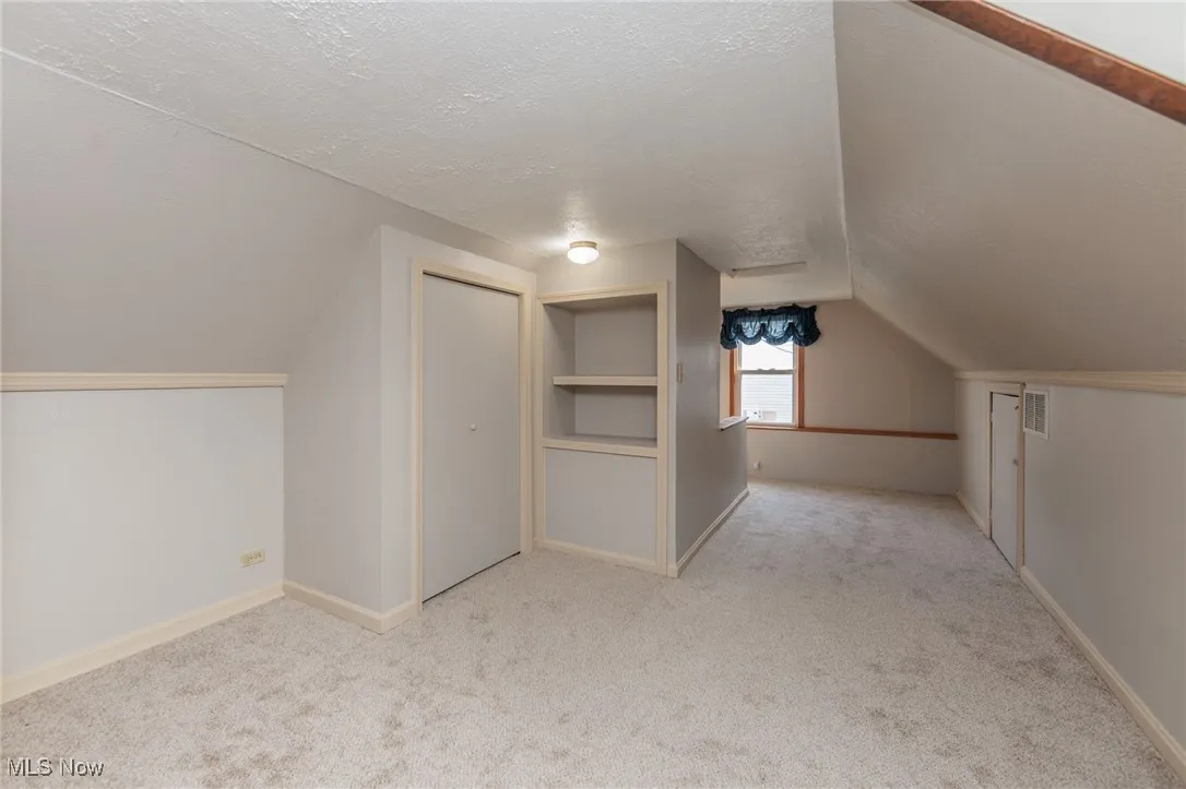 Bonus room with a textured ceiling, lofted ceiling, and light carpet