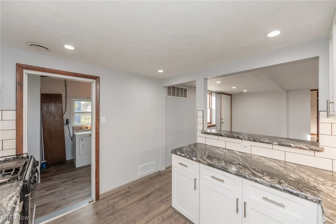 Kitchen featuring white cabinetry, dark stone counters, gas stove, dark wood-type flooring, and washer / clothes dryer