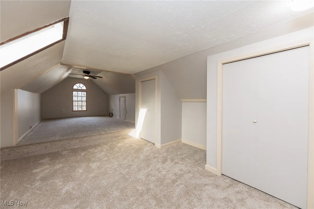 Bonus room featuring light carpet, vaulted ceiling, a textured ceiling, and a ceiling fan