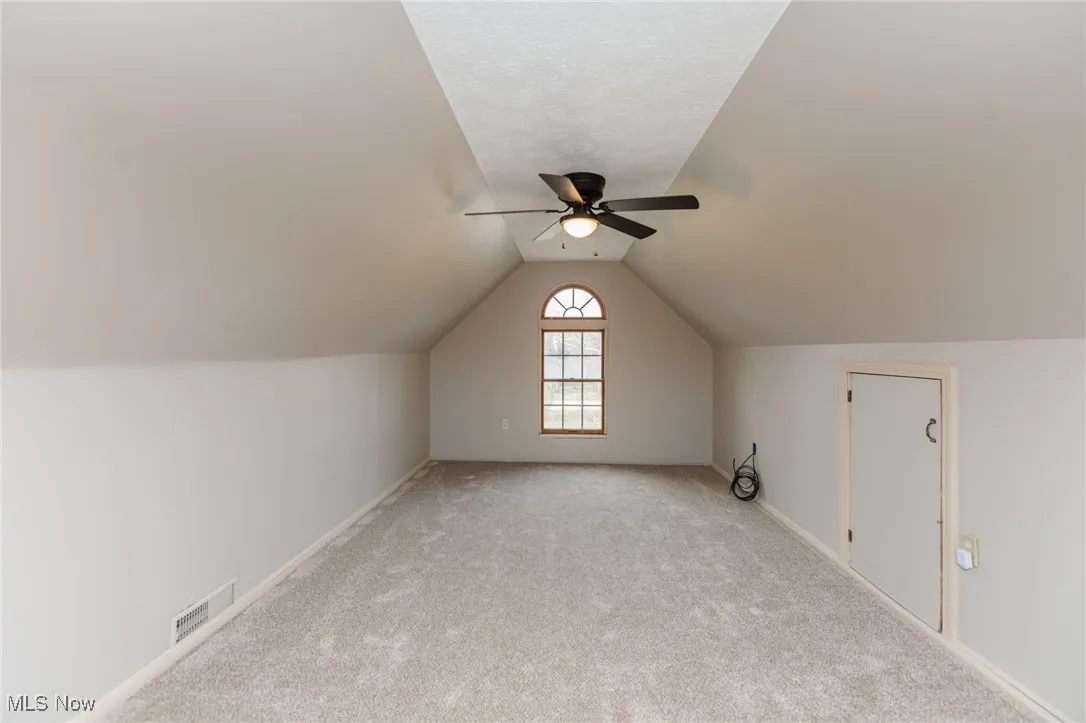 Additional living space with vaulted ceiling, carpet floors, a ceiling fan, and a textured ceiling