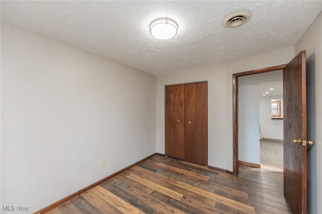 Unfurnished bedroom featuring dark wood finished floors, a closet, and a textured ceiling
