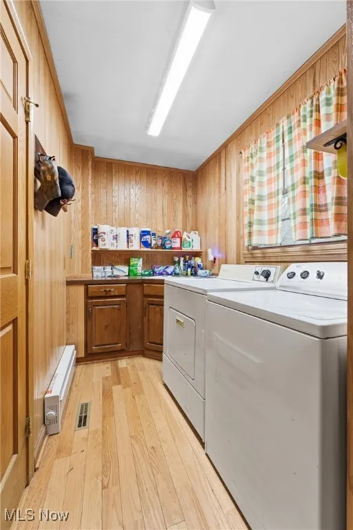 Laundry area featuring light wood finished floors, wood walls, and cabinet space