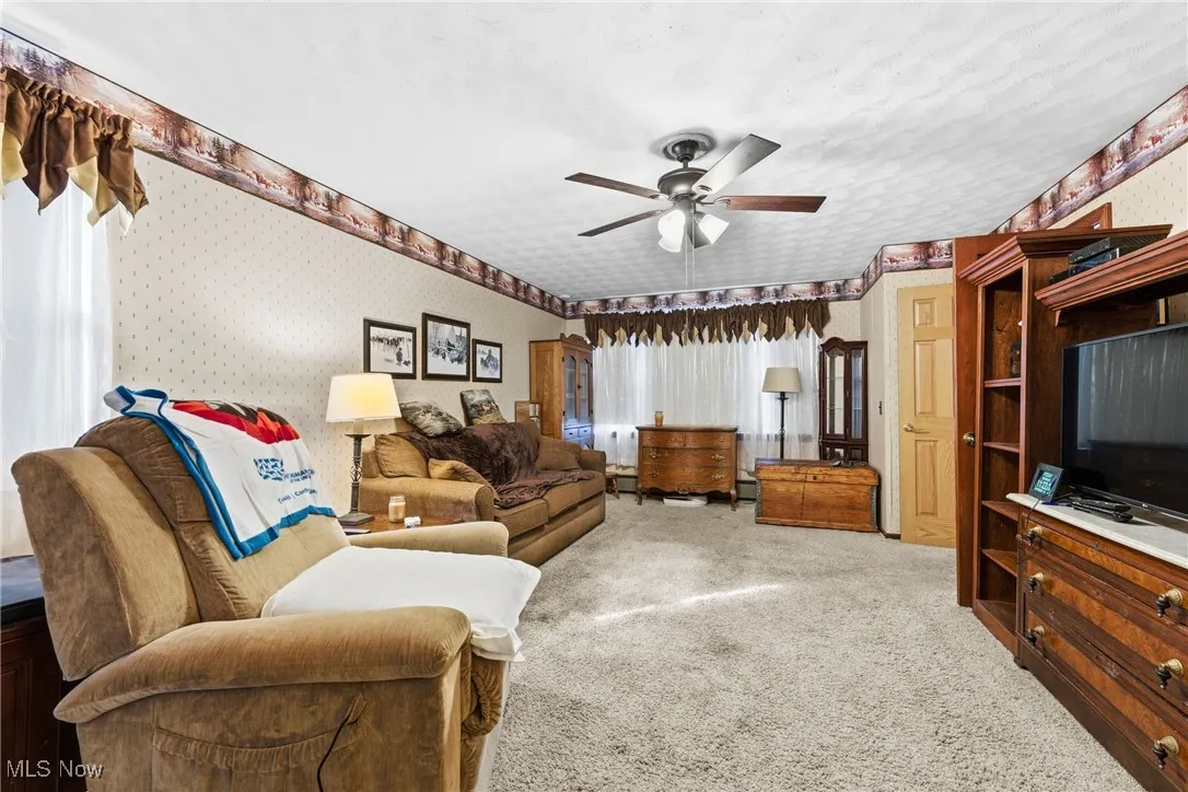 Living area featuring light carpet, wallpapered walls, and a ceiling fan