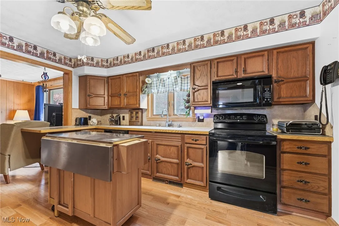 Kitchen with black appliances, brown cabinets, light countertops, and healthy amount of natural light