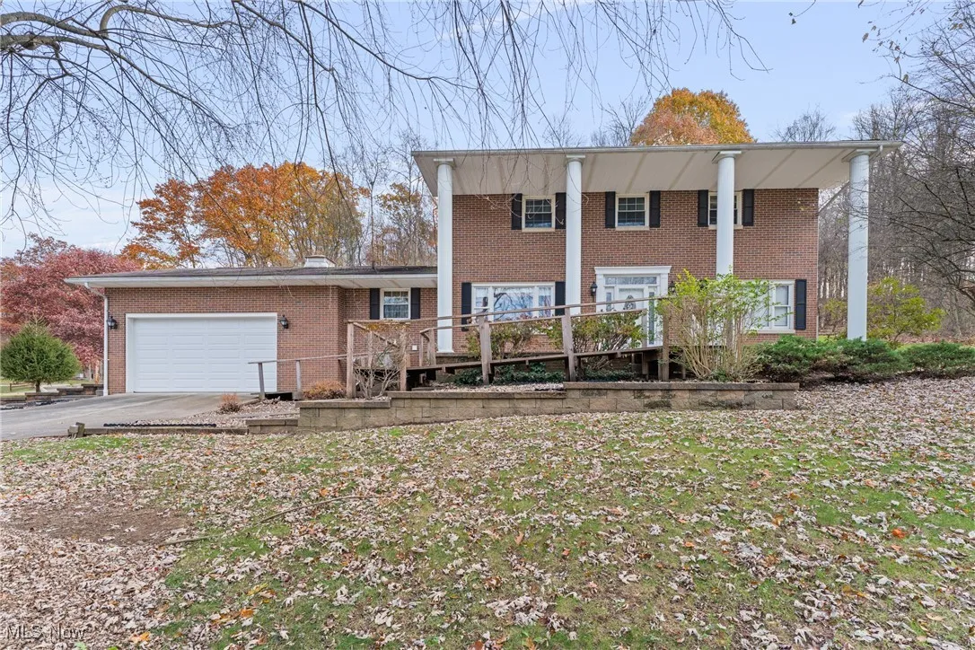 Neoclassical home with driveway, a garage, brick siding, and a deck