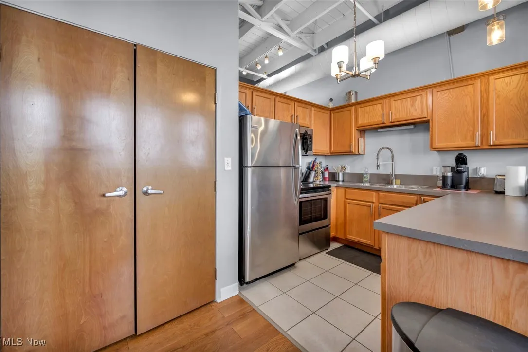 Kitchen featuring appliances with stainless steel finishes, pendant lighting, light wood-type flooring, a chandelier, and brown cabinetry