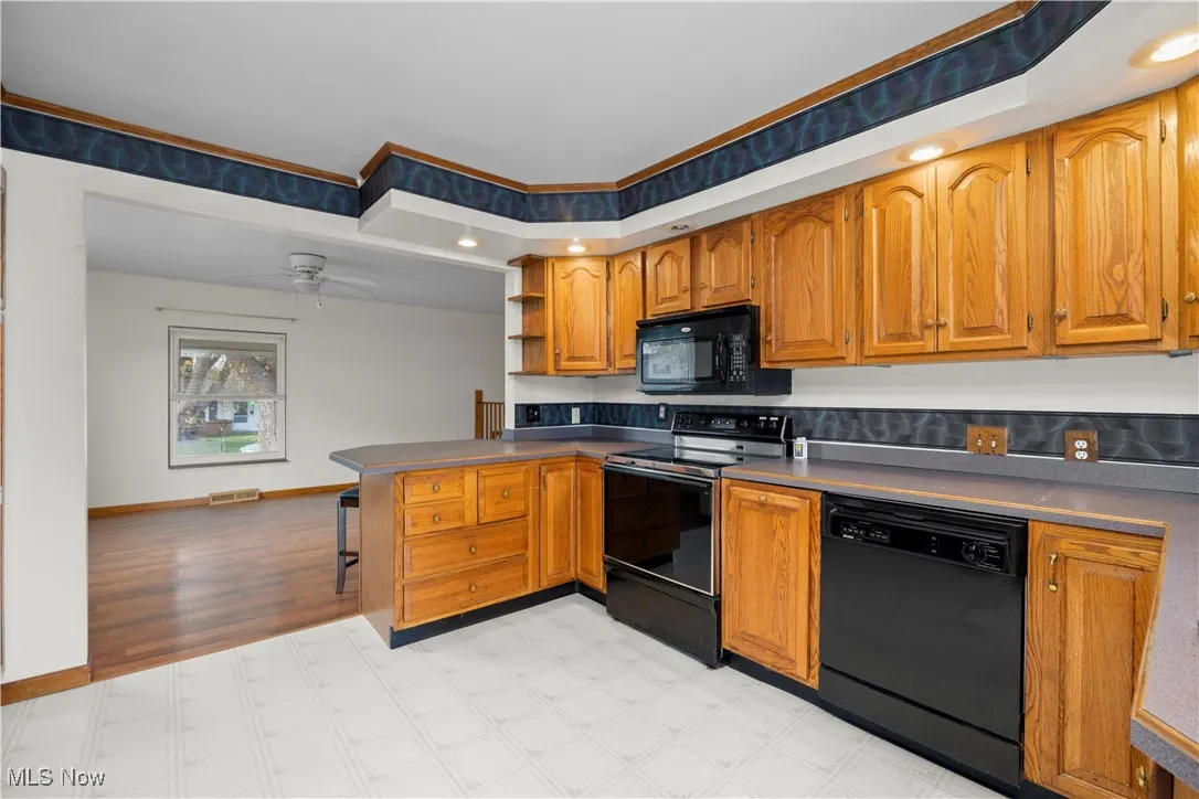 Kitchen featuring black appliances, brown cabinetry, open shelves, a peninsula, and ceiling fan