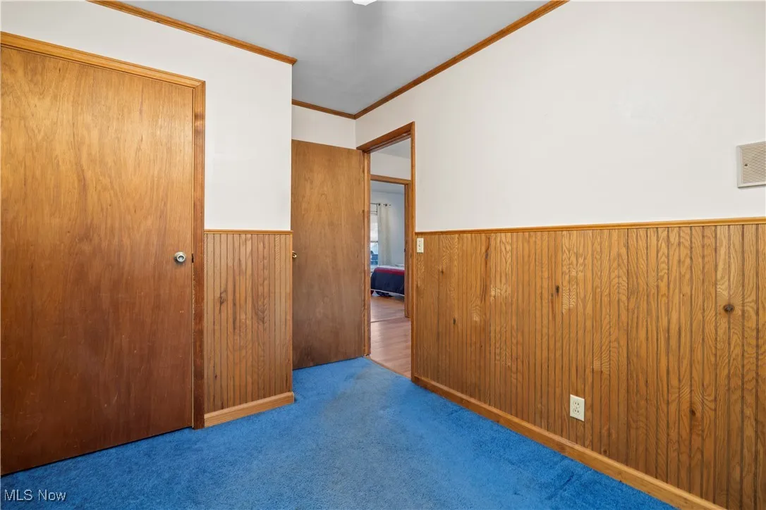 Unfurnished bedroom featuring a closet, ornamental molding, wainscoting, carpet floors, and wooden walls