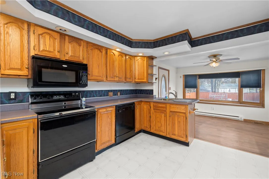 Kitchen featuring black appliances, brown cabinetry, light flooring, a peninsula, and a baseboard radiator