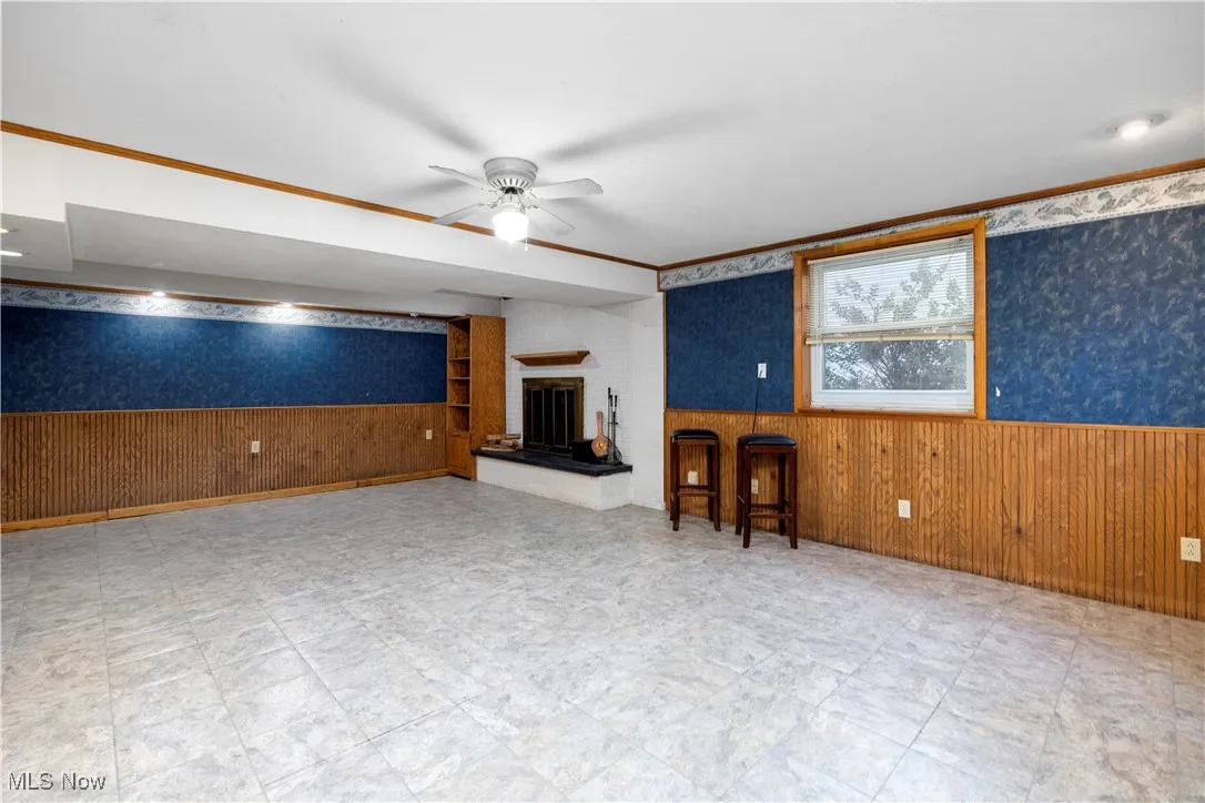 Unfurnished living room with a wainscoted wall, wood walls, wallpapered walls, ceiling fan, and crown molding