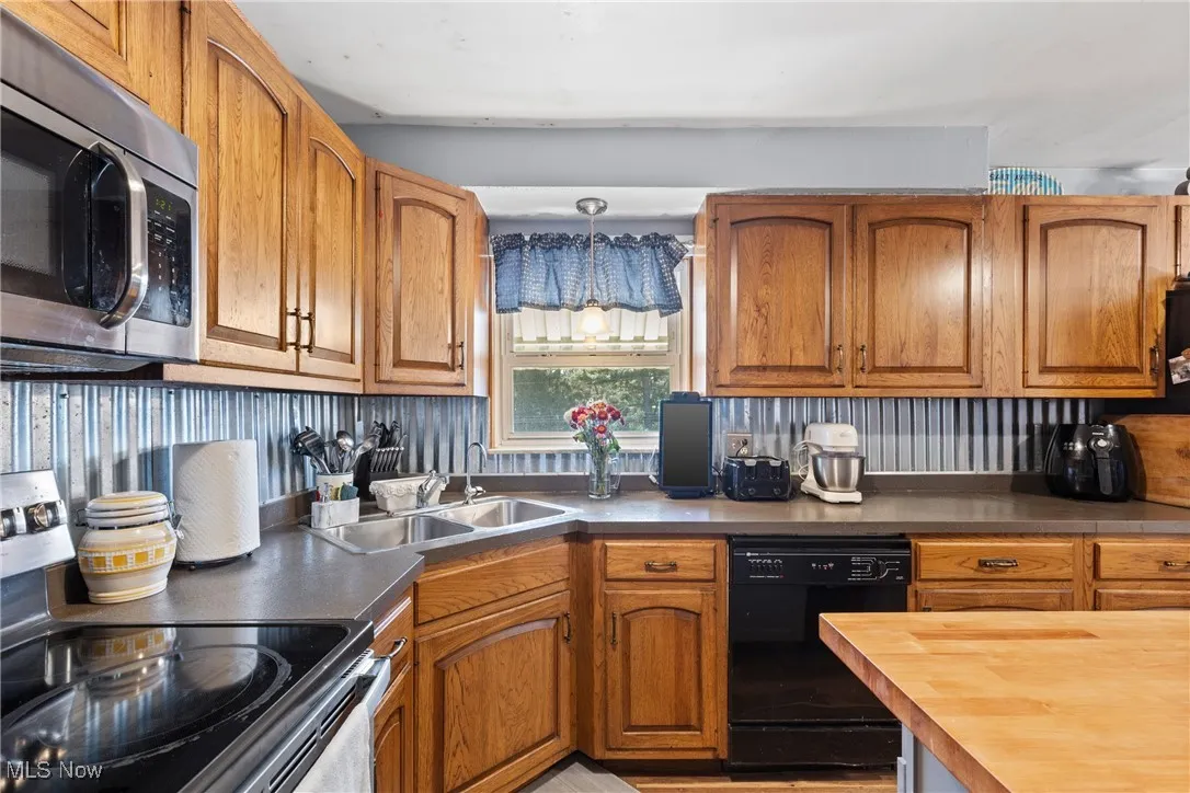 Kitchen featuring appliances with stainless steel finishes, brown cabinetry, butcher block countertops, and pendant lighting