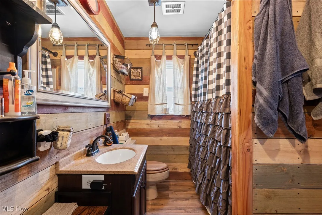 Bathroom with wood walls, curtained shower, wood finished floors, vanity, and plenty of natural light