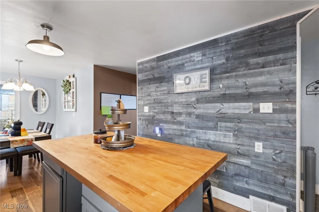 Dining space featuring wooden walls, dark wood-style floors, a chandelier, and an accent wall