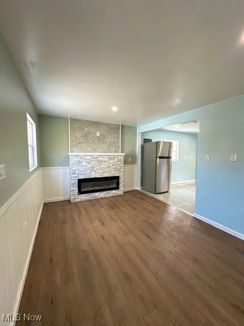 Unfurnished living room featuring dark wood-type flooring and a stone fireplace