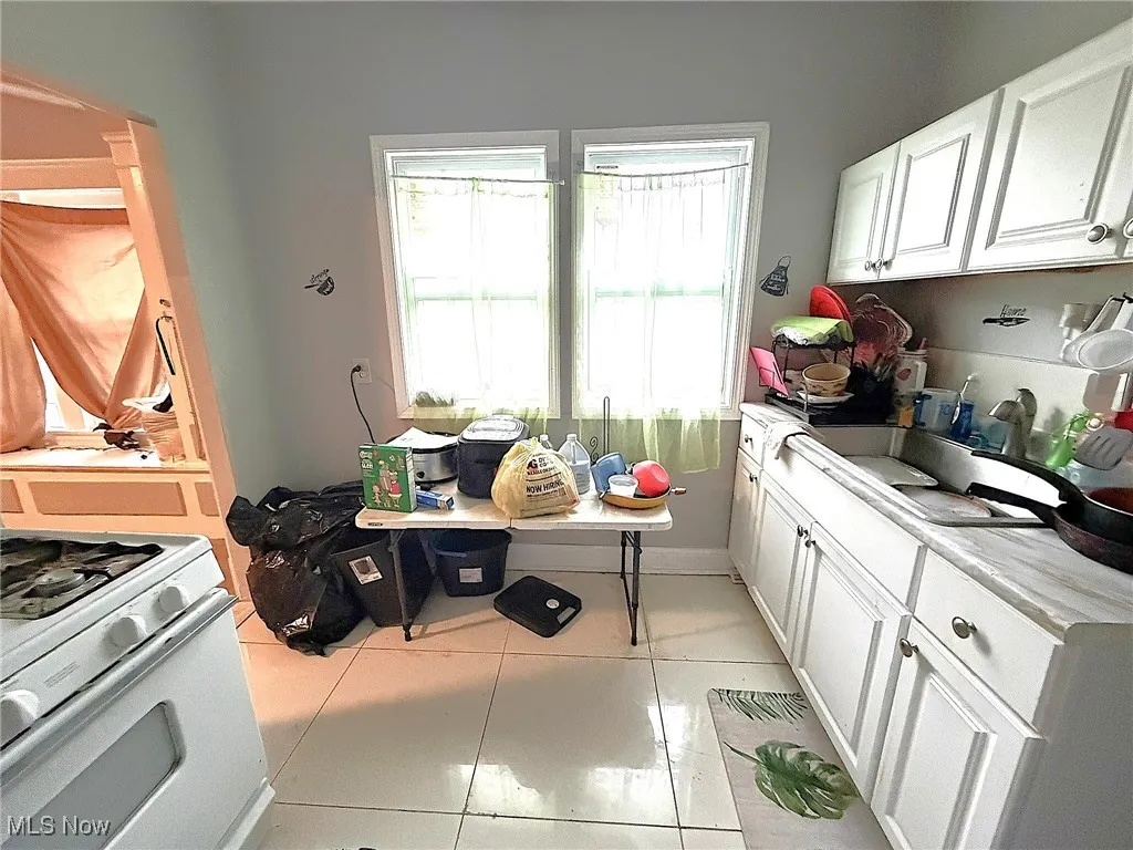 Kitchen with white cabinets, light countertops, light tile patterned floors, and gas range gas stove