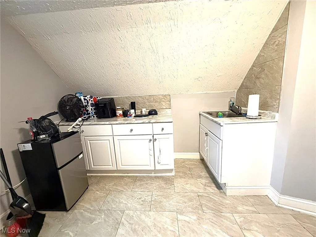Third level kitchen/unit with light countertops, freestanding refrigerator, white cabinetry, lofted ceiling, and a textured ceiling