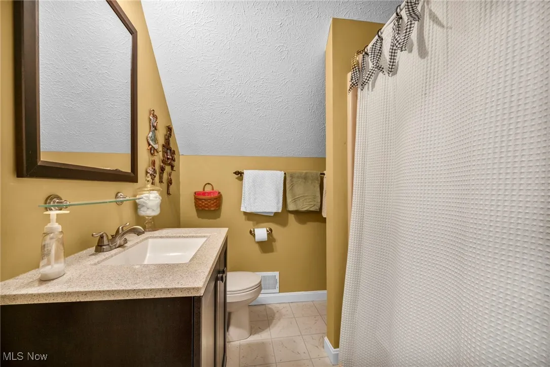 Full bath featuring a textured ceiling, vanity, lofted ceiling, and curtained shower